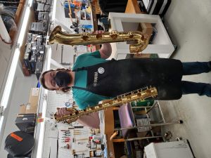 David standing, holding a baritone saxophone body and bell